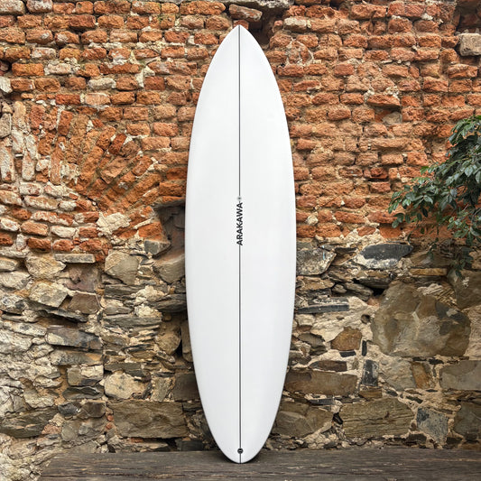 White Arakawa surfboard in front of a stone wall.
