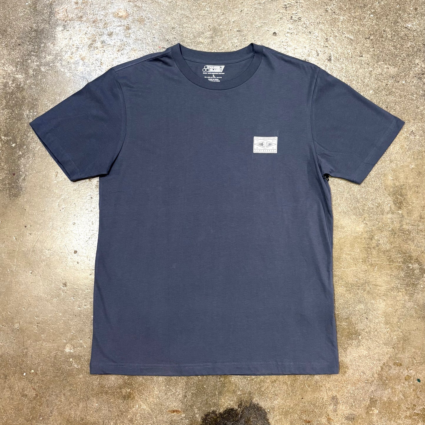 Navy blue Channel Islands t-shirt with a small white logo on a textured beige surface
