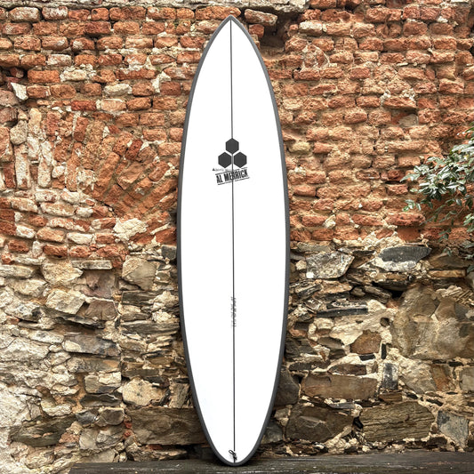 White CHANNEL ISLANDS   M23   6’6"  20 1/2"  2 11/16"   39.4L surfboard with a logo against a rustic stone wall