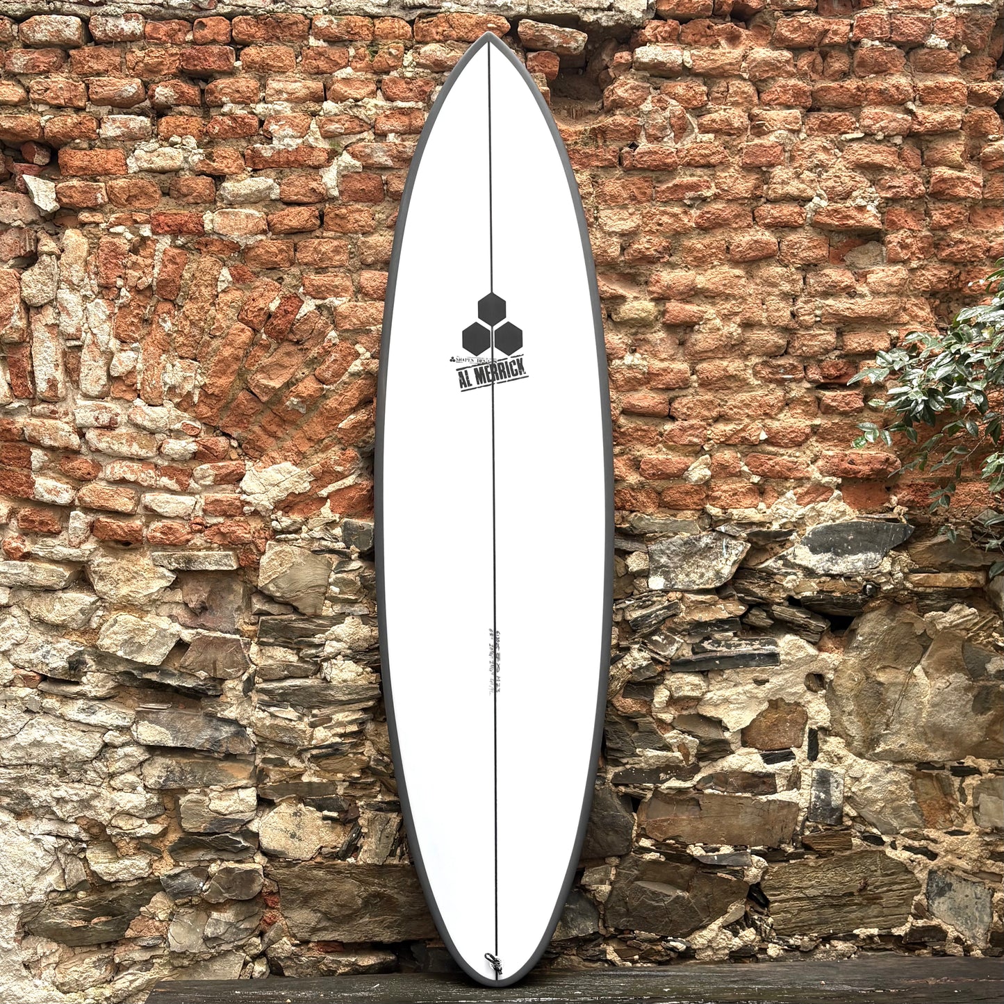 White CHANNEL ISLANDS M23 6’8" 20 3/4" 2 3/4" 41.8L surfboard with a logo against a rustic stone wall
