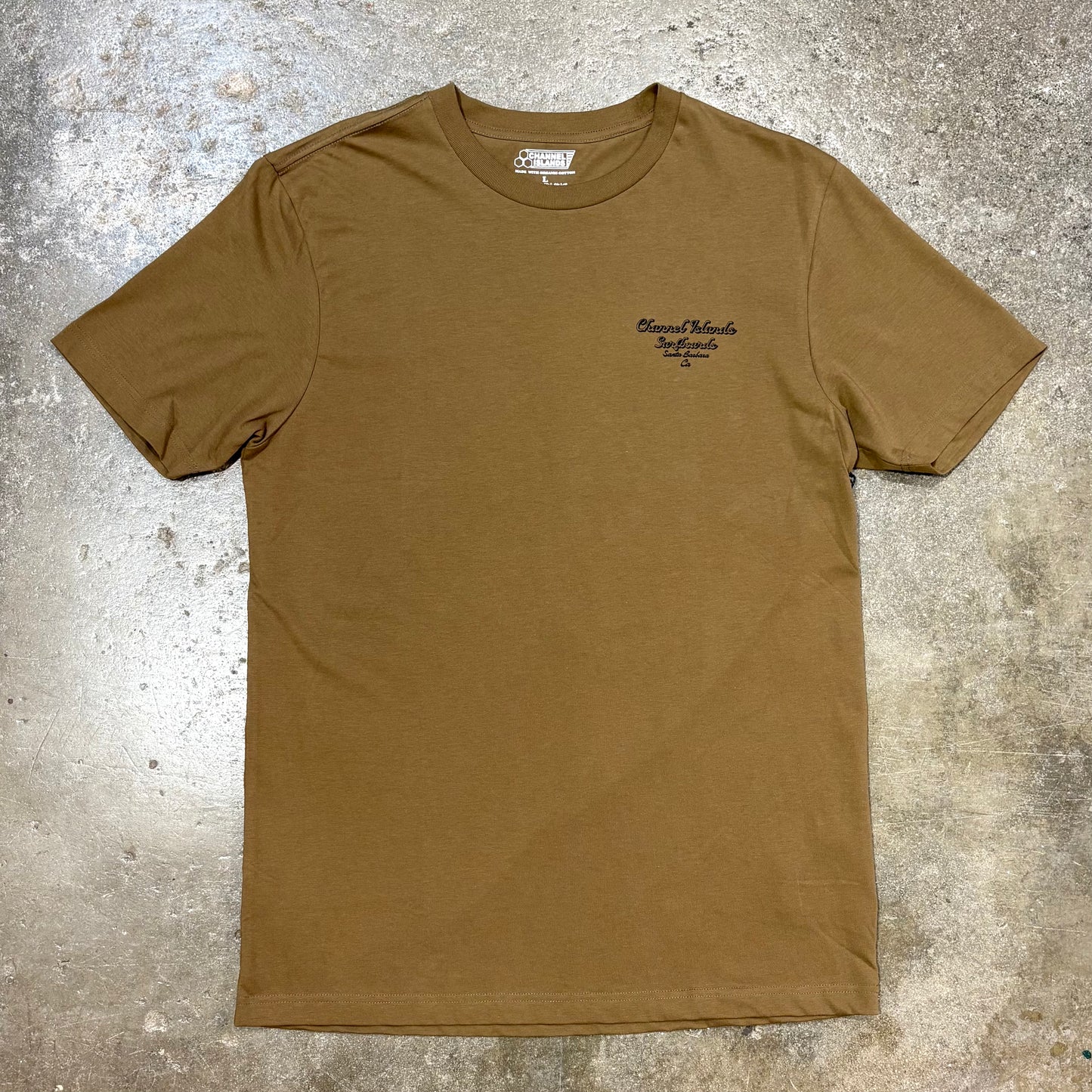 Brown Channel Islands T Shirt with logo in left corner on a concrete surface