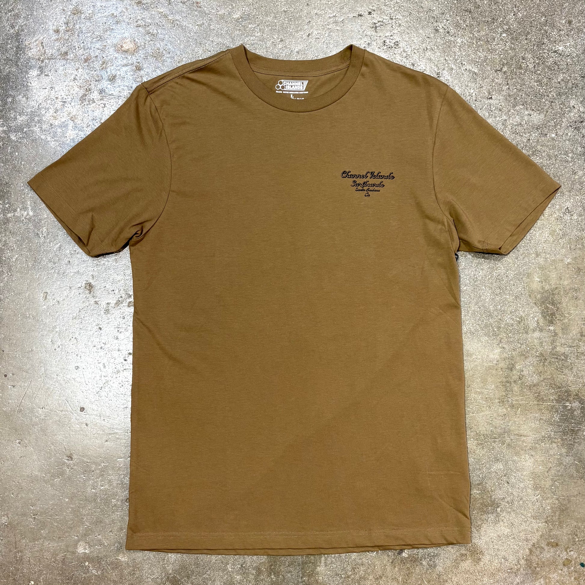 Brown Channel Islands T Shirt with logo in  left corner on a concrete surface