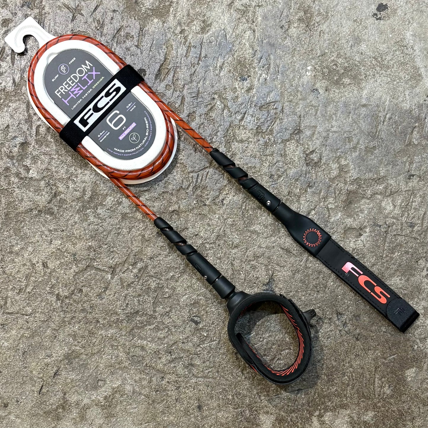 A FCS Freedom Helix Leash - All Round in red lying on a concrete floor
