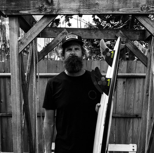 Britt Merrick holding a surboard with a FCS II Al Merrick PG Pro Tri Fin Set in