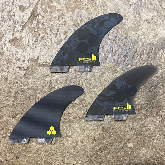 A set of the FCS II Al Merrick PG Pro Tri Fin laid out to see. Black, grey and yellow colour way