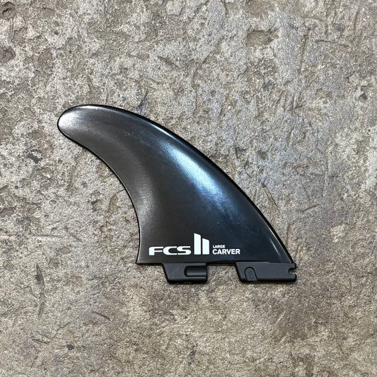 A single fin from the FCS II Carver Glass Flex Tri Fins in the black colour way laid out on a concrete surface