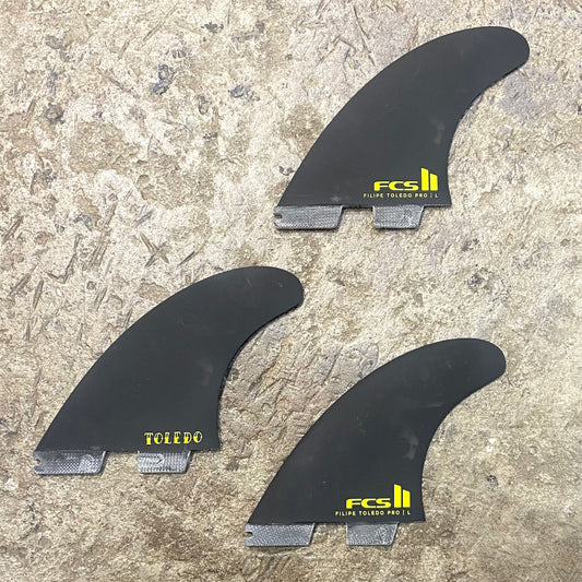 View of the FCS II Filipe Toledo PG Pro Tri Fin Set laid out on a concrete floor