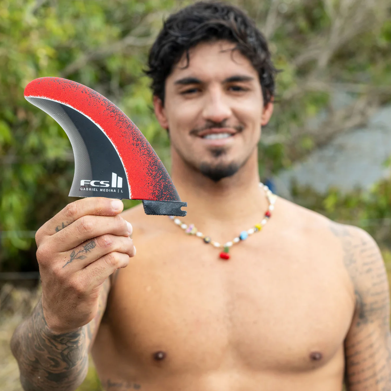 Gabriel Medina holding a FCS II Gabriel Medina Signature Tri Fins with red, black, and grey color scheme.