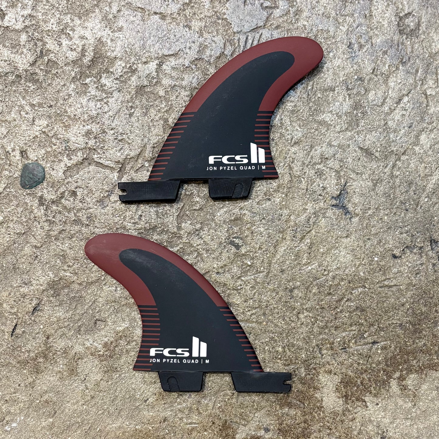 Two FCS II surfboard fins on a textured surface