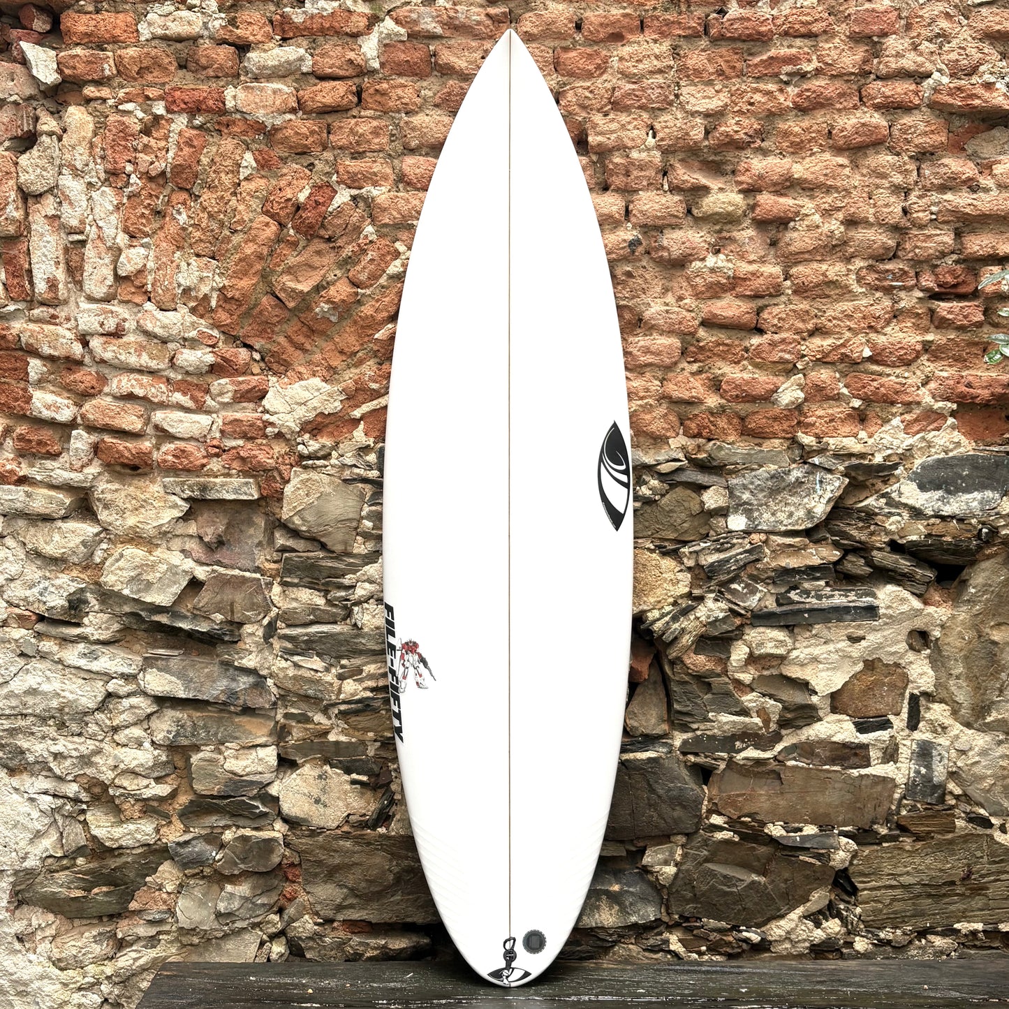 White File Fifty 5'9" x 18.88 x 2.42 27.08L surfboard with a logo against a rustic stone wall