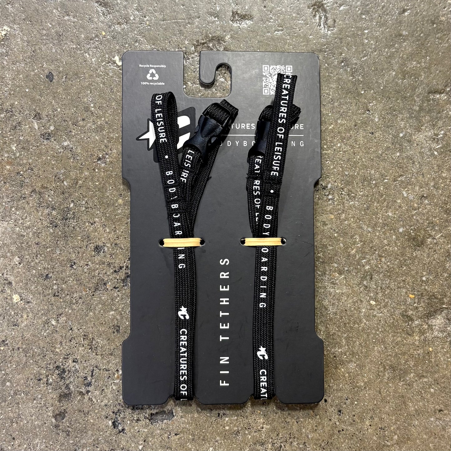 Two black fin tethers on a gray card with text on a concrete surface