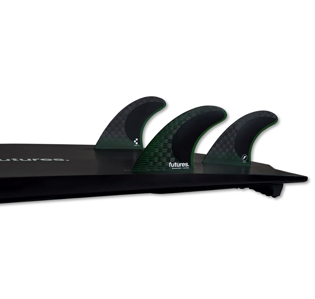 A set of Futures F8 Blackstix black and green surfboard fins displayed in a black surfboard against a white background