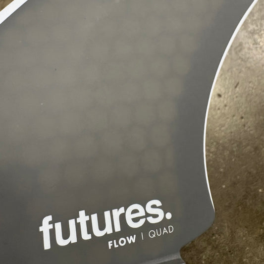 Close-up of a Futures Fin with 'Flow Quad' text on a textured surface.