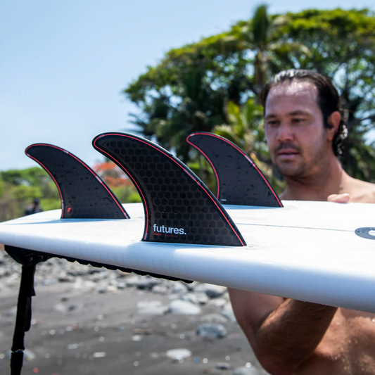Jordy Smith holding a surfboard with the Futures Jordy Signature fins, in a red and black colour way.