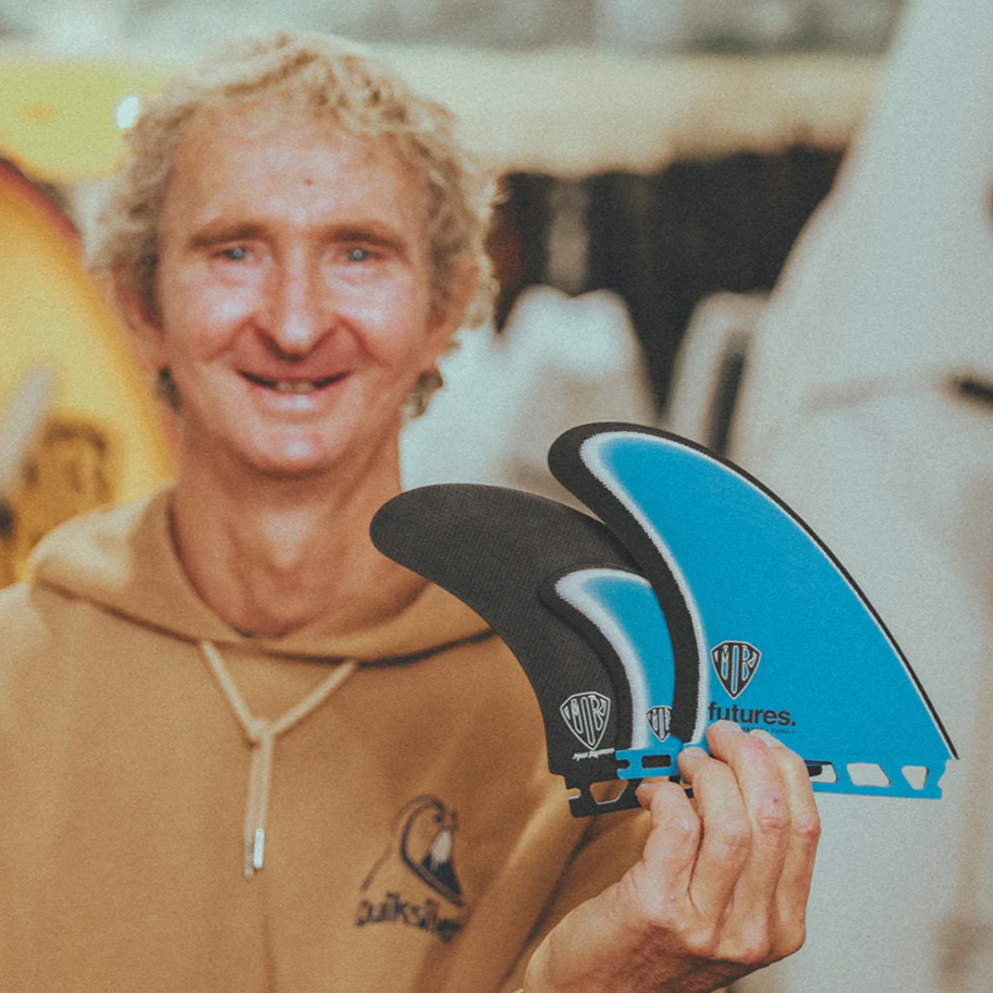 Mark Richards holding two of his signature surfboard fins with a blurred background