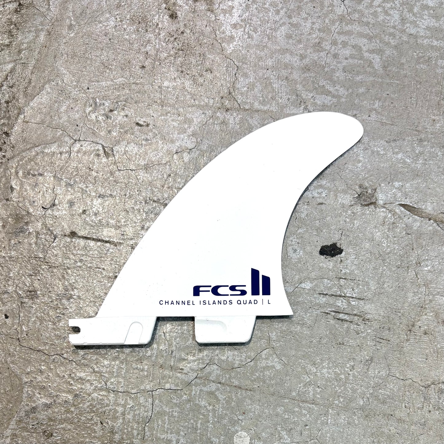 White surf fin with FCS logo on a textured gray surface