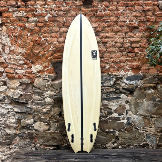 White surfboard with black accents against a rustic stone wall.