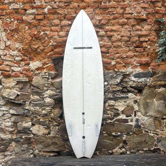 A white surfboard standing upright against a rustic brick and stone wall.