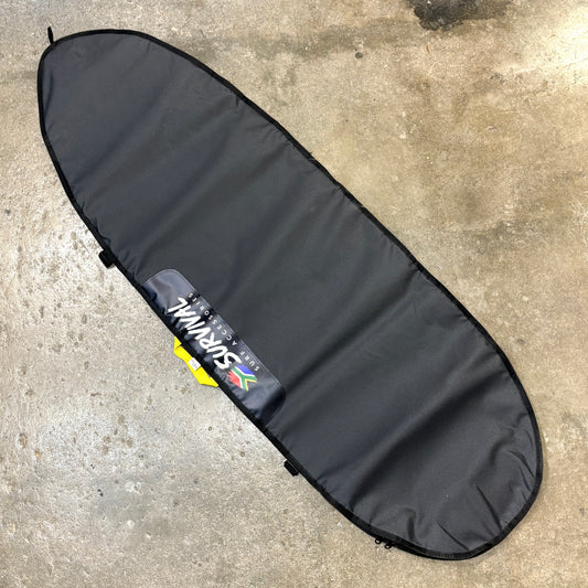 A black surfboard carrying bag laid diagonally on a concrete floor, featuring a visible Survival brand patch.