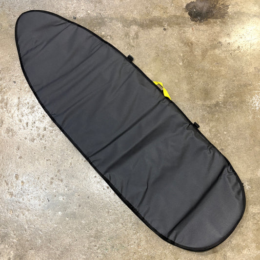 A black surfboard carrying bag laid diagonally on a concrete floor, with a small yellow loop visible near the upper right side.