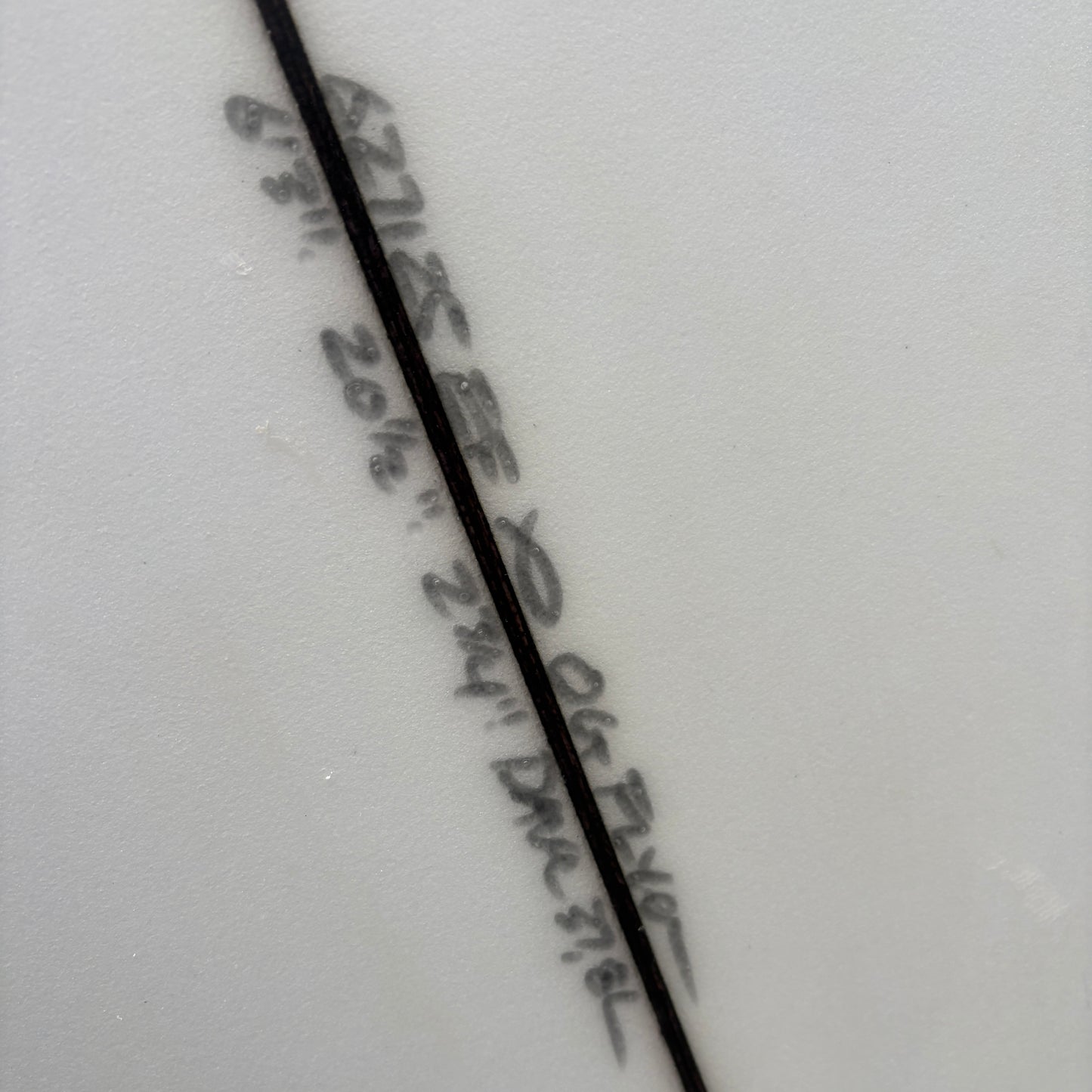 Close-up of a white ceramic surface with a diagonal black line and dark printed text running parallel to it.