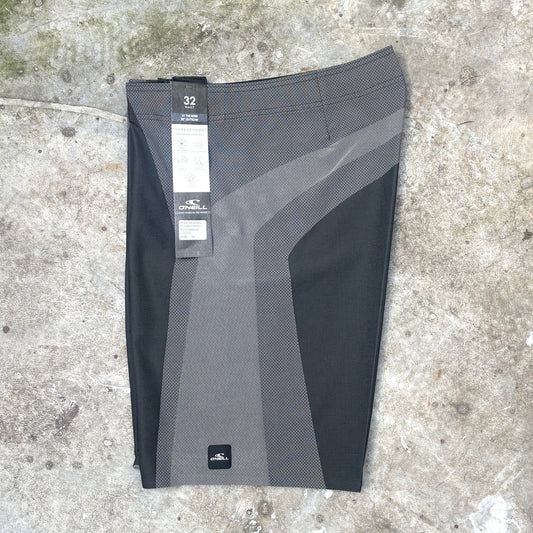 A pair of O'Neill athletic shorts in black and gray, laid flat on a concrete surface. The shorts feature a textured mesh pattern and a black waistband, with retail tags still attached.