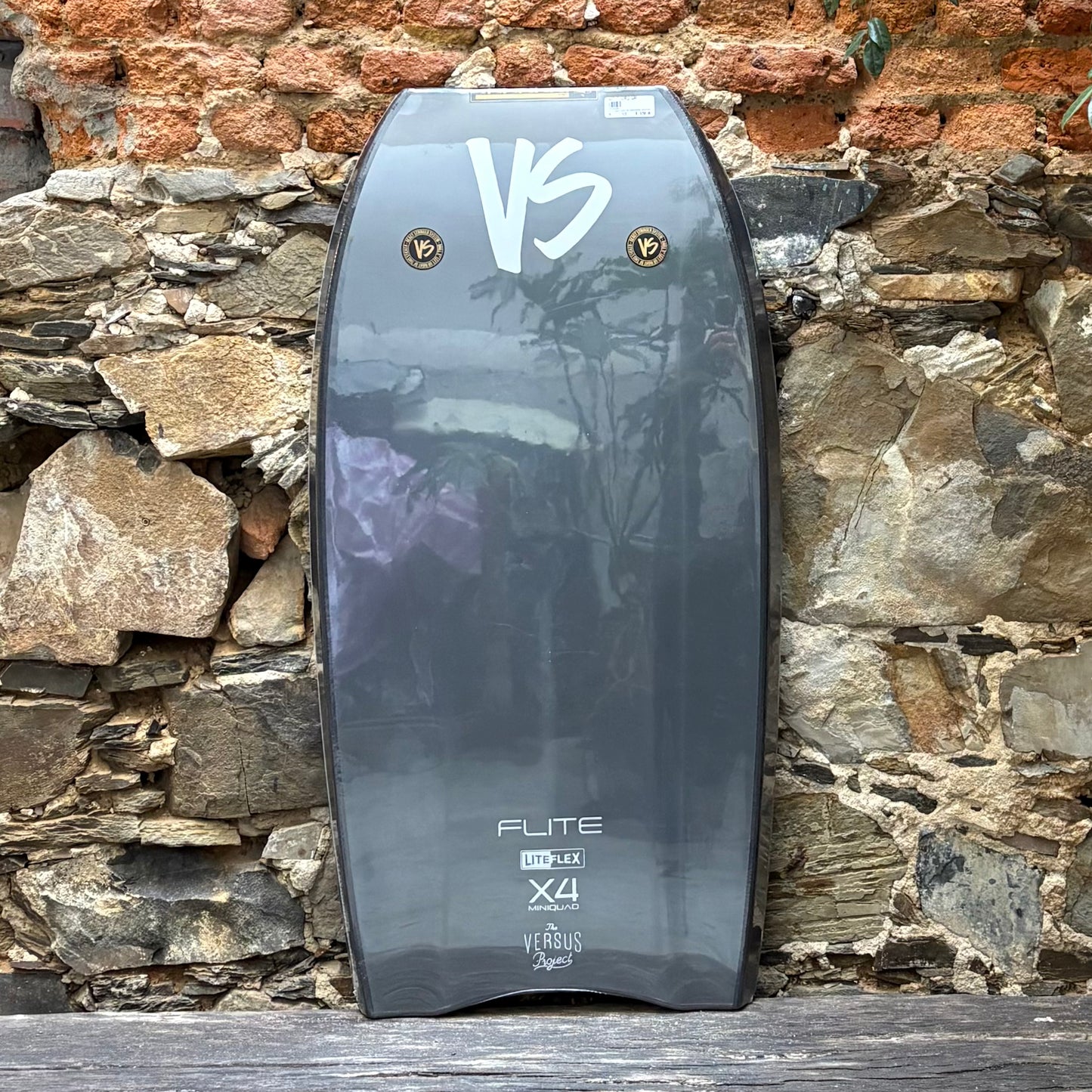 Bodyboard with 'VS' branding against a stone wall