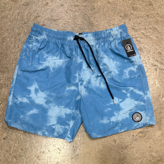 Blue Volcom tie-dye shorts with a brand label on a beige surface