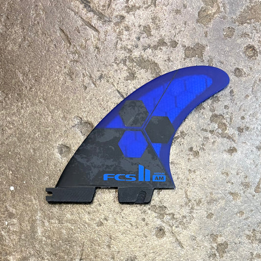 Blue and black FCS surfboard fin on a textured surface