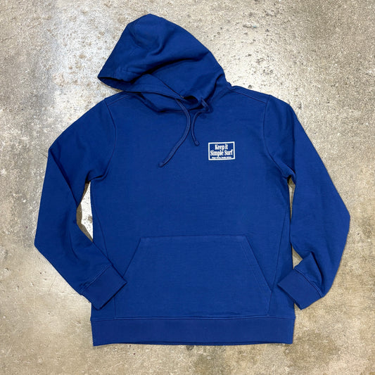 A royal blue pullover hoodie with a small white embroidered 'keep it local' logo on the left chest, laid flat on a textured concrete surface.
