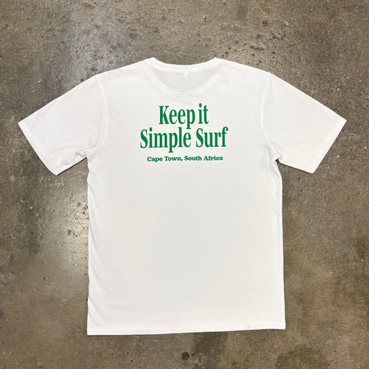 White t-shirt with green text 'Keep it Simple Surf Cape Town, South Africa' on a concrete surface