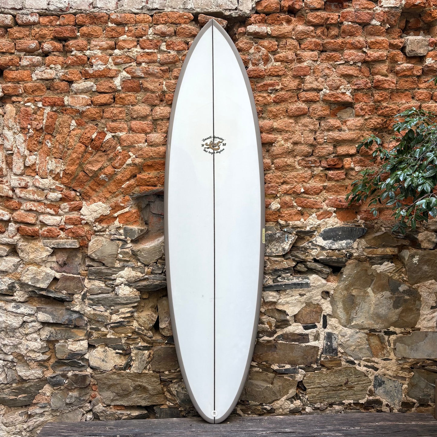 White surfboard leaning against a rustic stone wall.