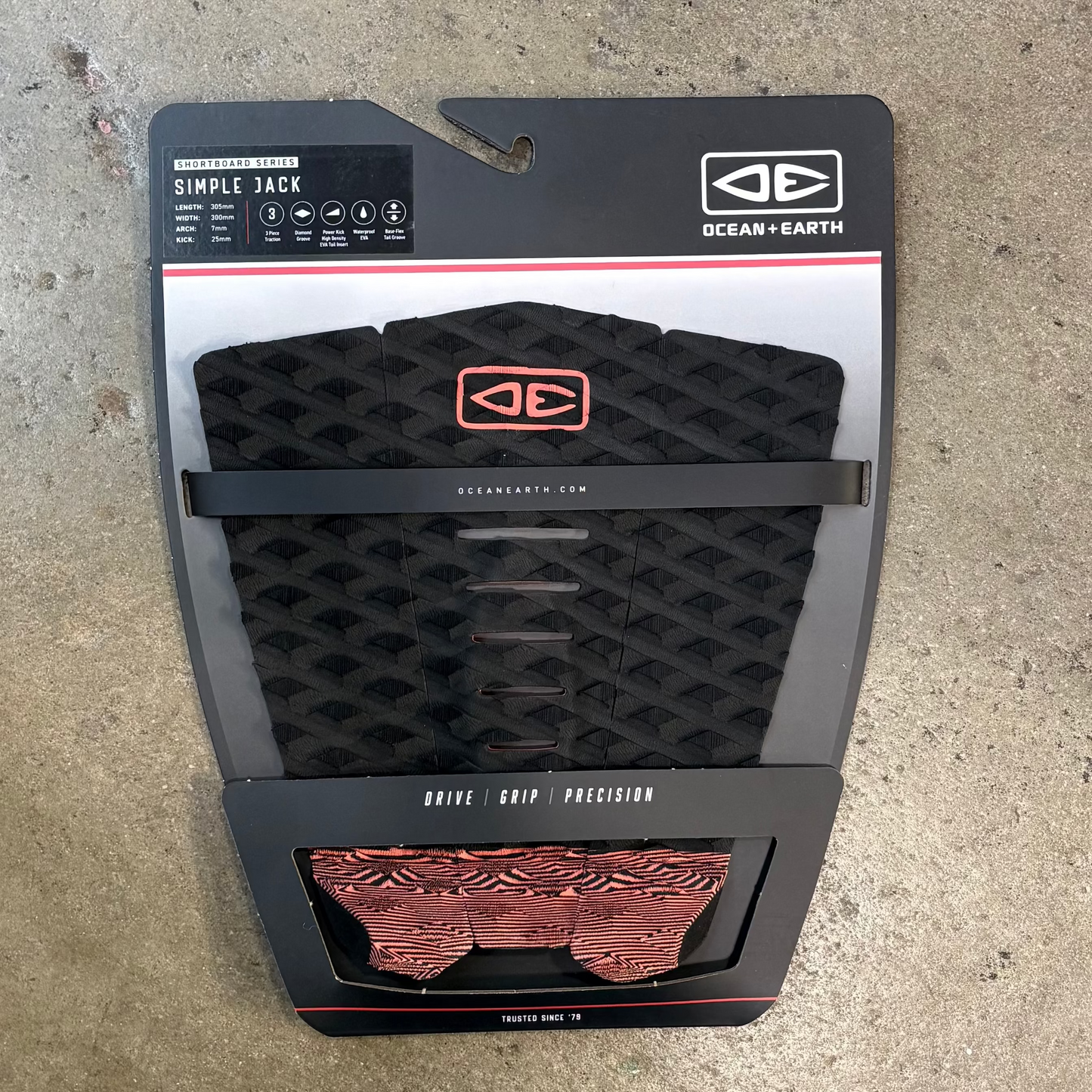 Black and red surfboard leash pad with Ocean and Earth branding on a concrete surface