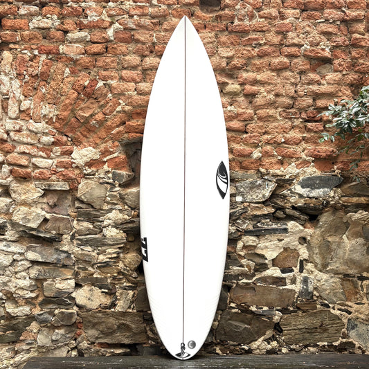 White SHARPEYE #77 surfboard leaning against a rustic stone wall.