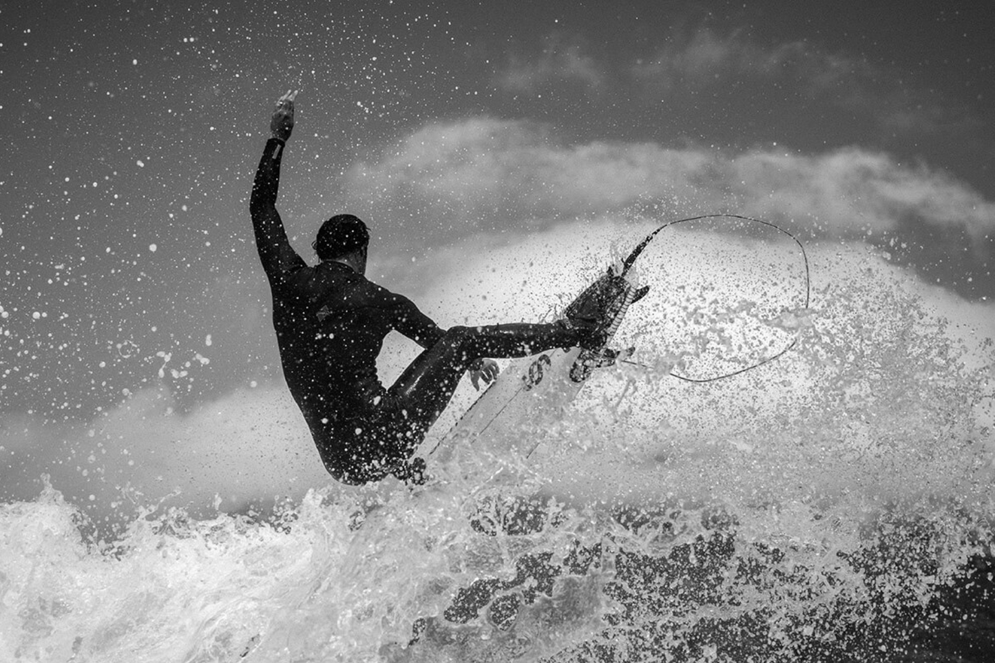Black and white photo of a Jordy Smith riding a wave with a dramatic sky.