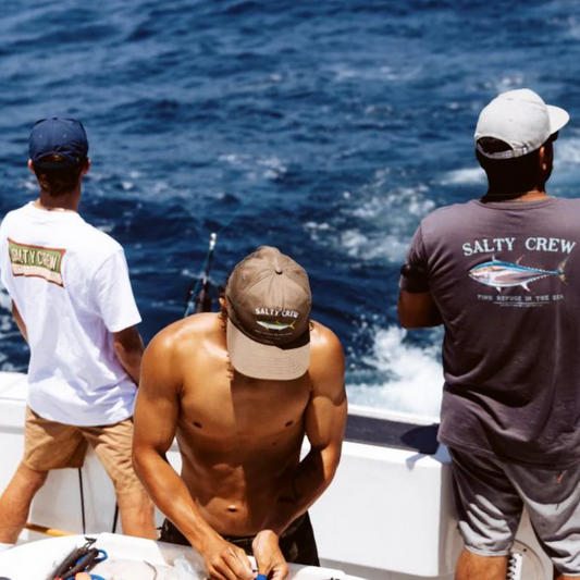 Three men on a boat wearing Salty Crew branded clothing, looking out at the ocean.