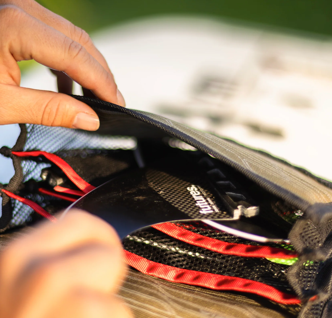 Close-up of a person's hands opening a black mesh storage pouch to reveal a carbon-fiber-textured item with red trim inside.
