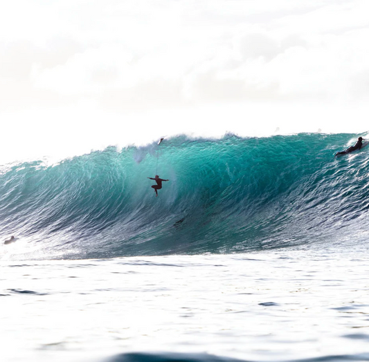 Surfer riding a large wave in the ocean with a clear sky.