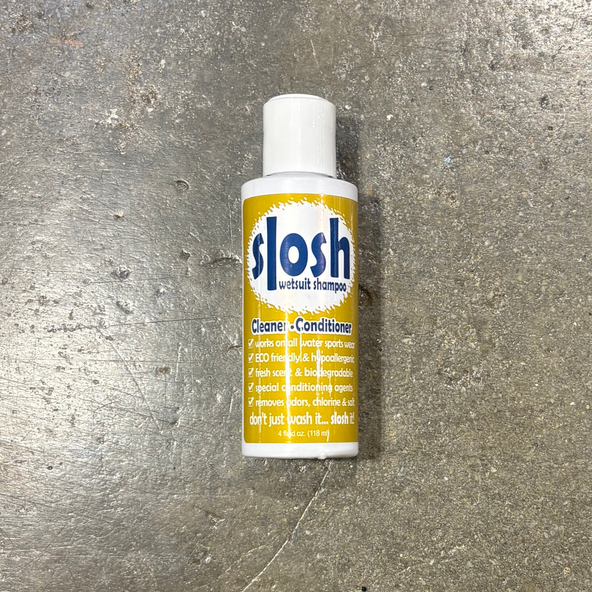 A bottle of slosh withhair shampoo cleaner and conditioner placed on a textured gray concrete surface. The bottle is white with a yellow label and blue slosh branding.
