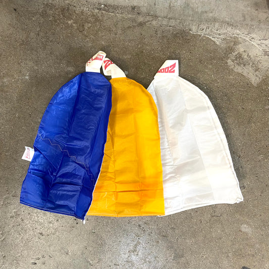 Three Zoomie wetsuit socks laid out on a concrete surface, with colours blue, yellow, and white, each featuring a red and white stripe design.