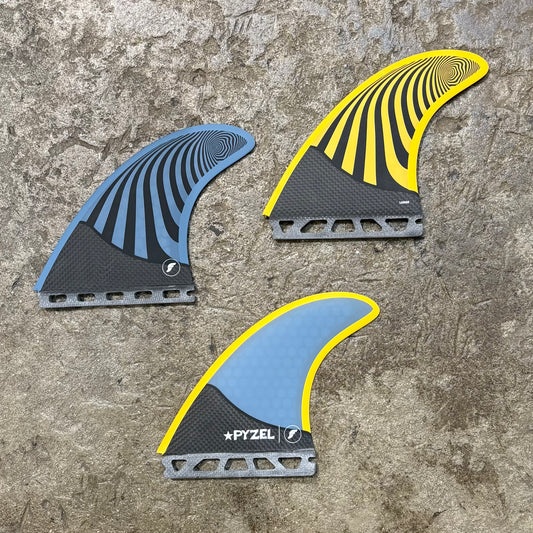 A set of three surfboard fins with a honeycomb structure and carbon fiber at the base, featuring blue and yellow coloration and the brand name 'Pyzel'.