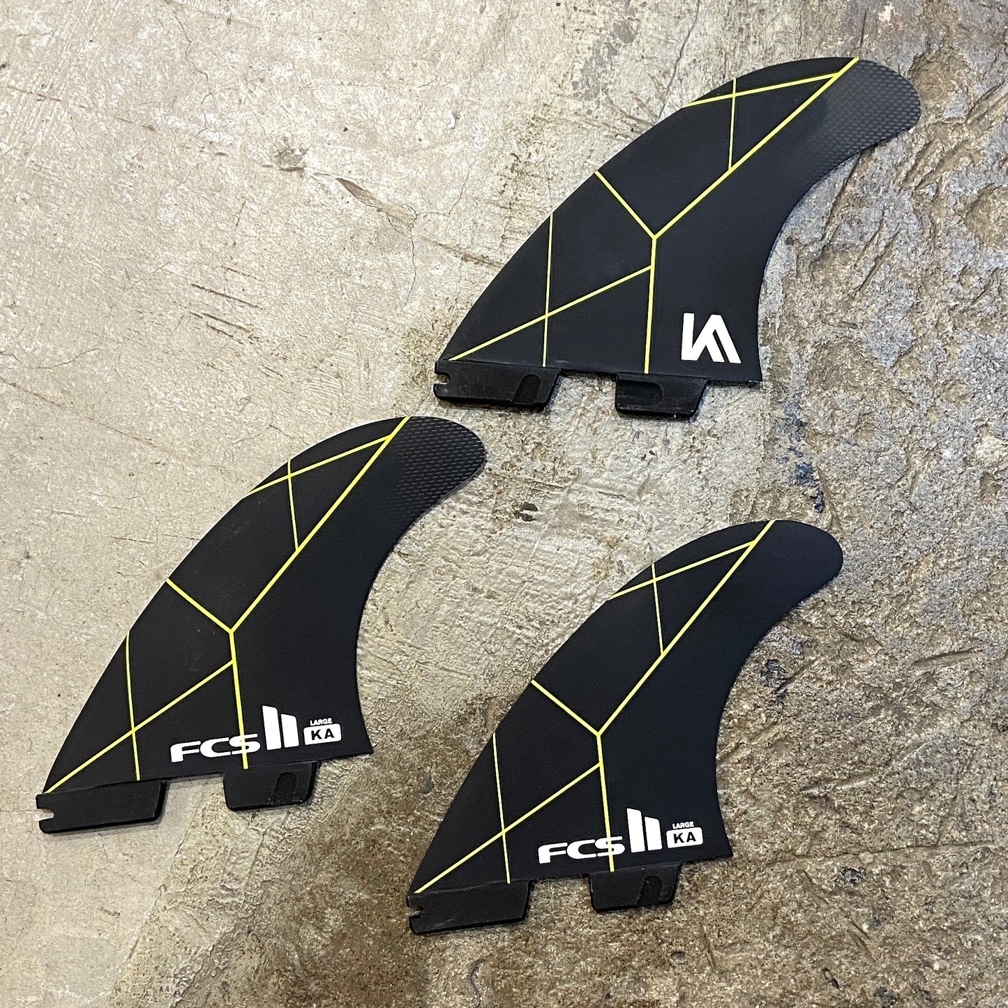 A set of large FCS ll Kolohe Andino PC Tri Set in a black colour way with green details laid on a concrete surface