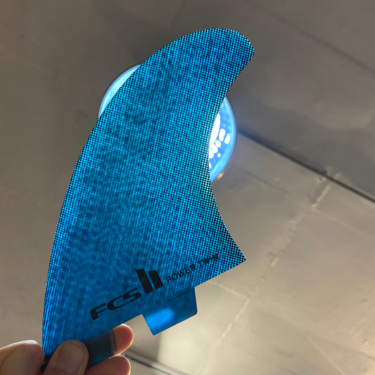 A set of FCS ll Power Twin Fins held up with a light behind it to show the blue colour way.