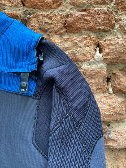 Detailed view of the zip closure on the O'Neill Youth Hyperfreak 4/3mm+ Chest Zip against a brick wall- Black and Blue - Kid's wetsuit