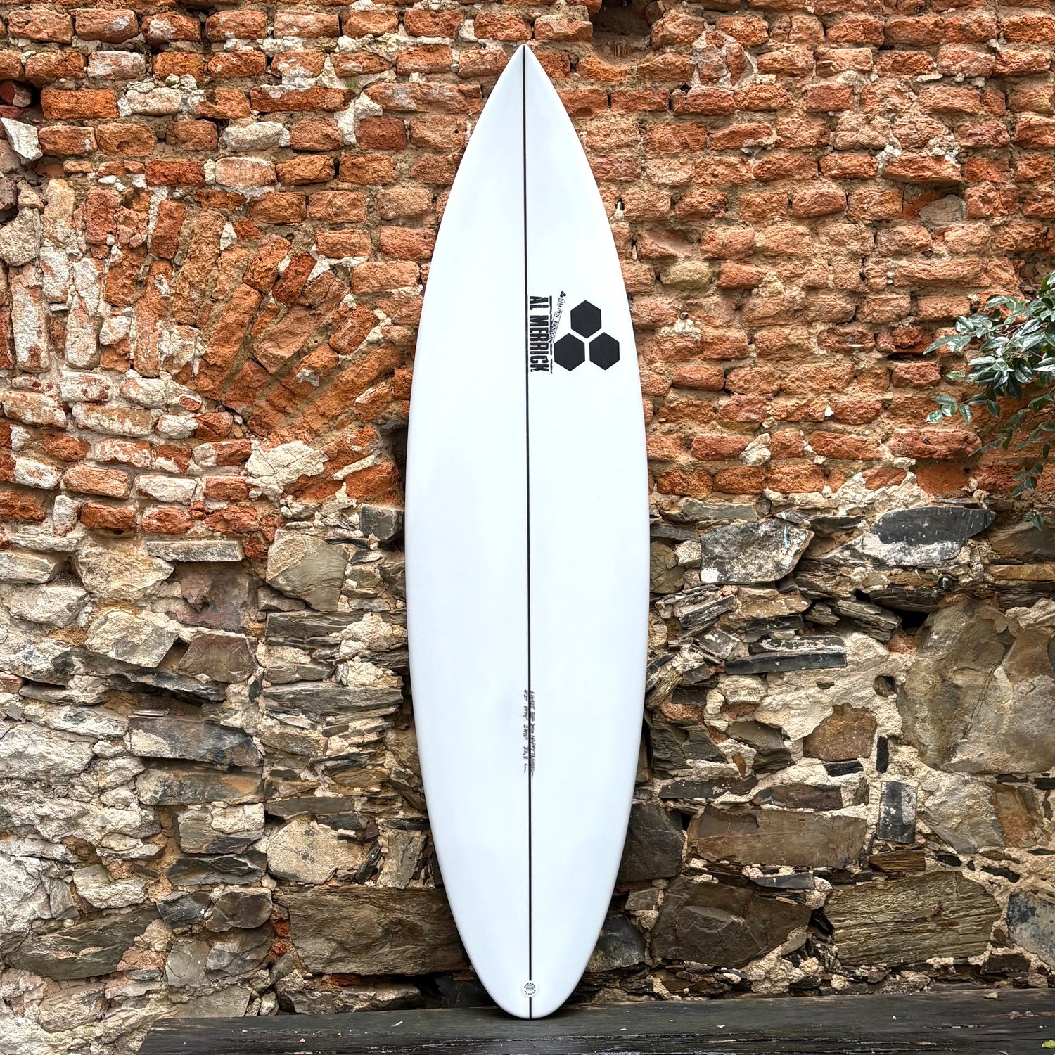 White surfboard leaning against a rustic stone wall.