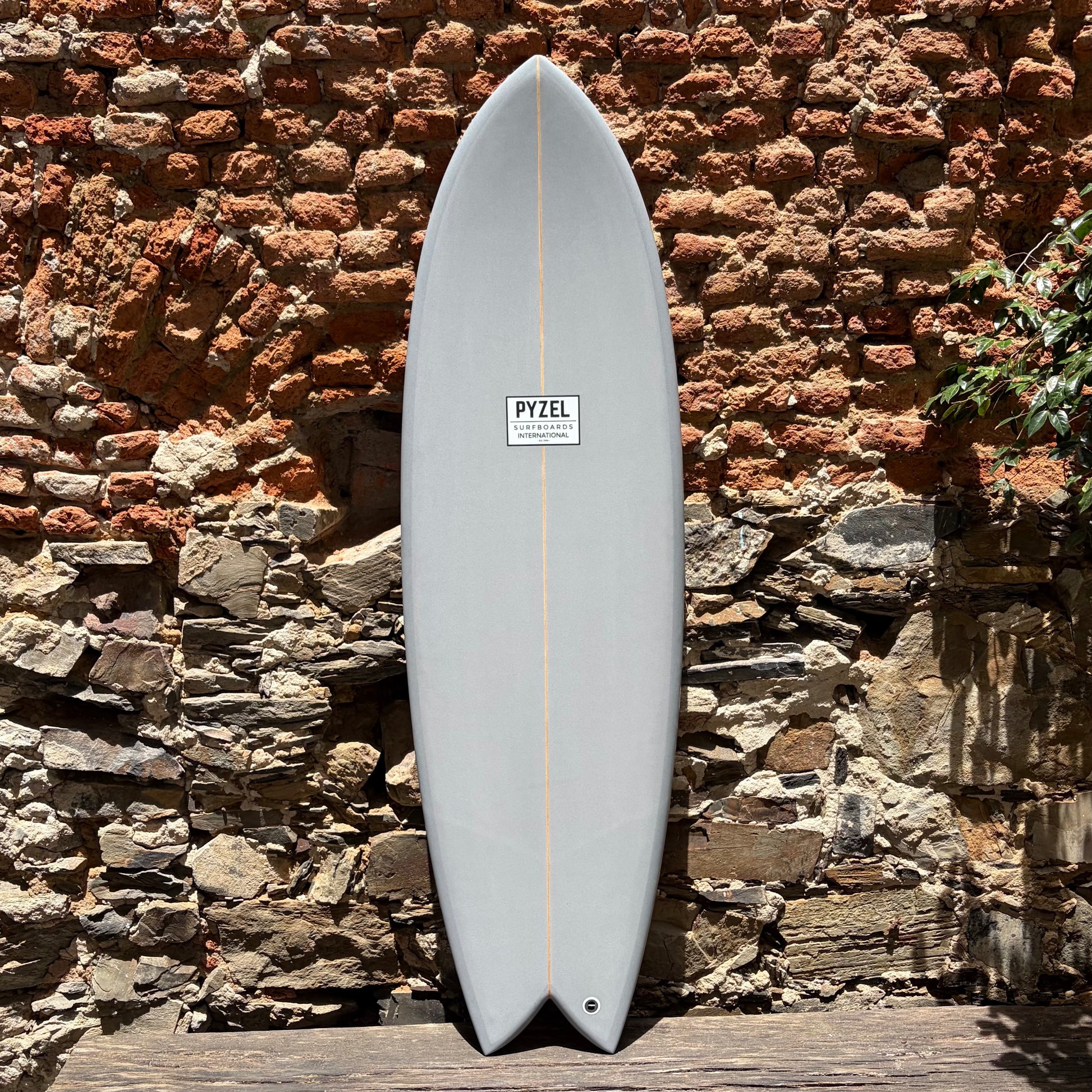 Surfboard with a visible Pyzel brand logo against a stone wall.