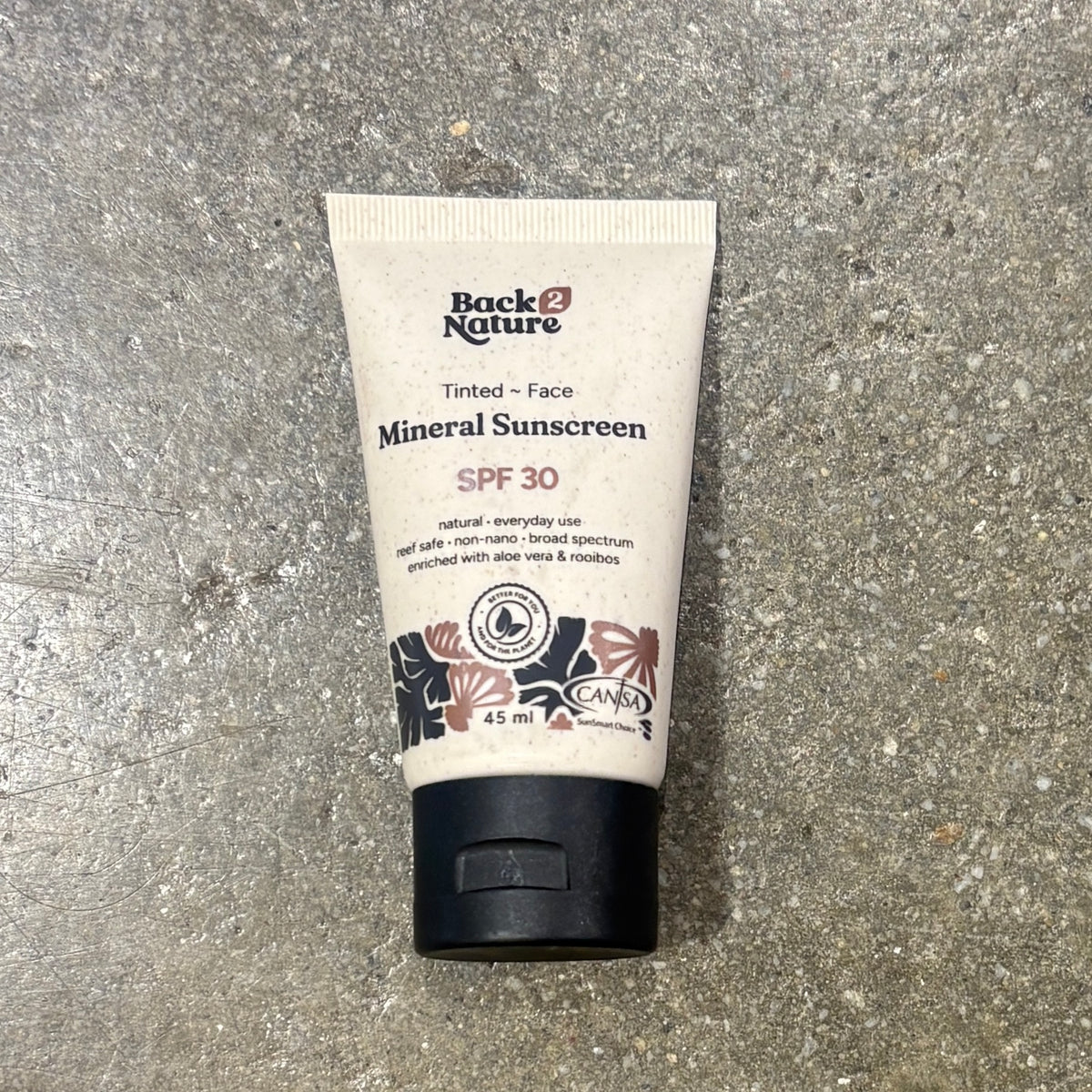 A 45 ml squeeze tube of Back Nature Tinted Face Mineral Sunscreen SPF 30, lying on a textured gray concrete surface.