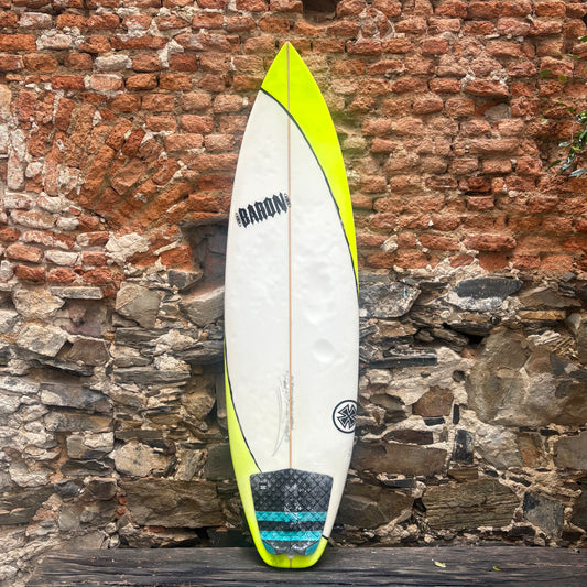 Surfboard with a visible brand logo against a rustic stone wall.