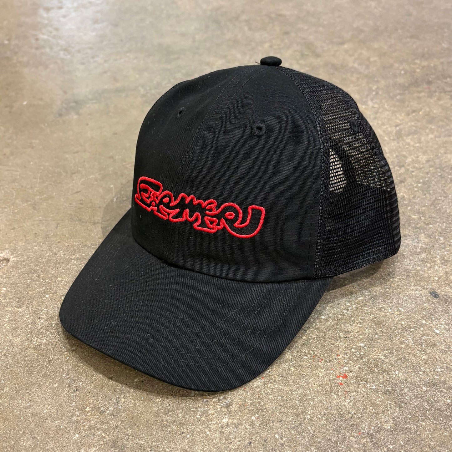 Black cap with red logo on a concrete surface