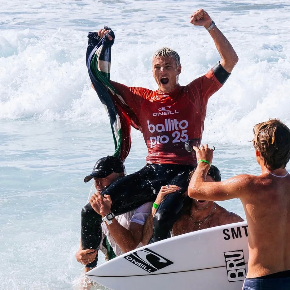 Surfer celebrating a victory with arms raised on a surfboard in the ocean.